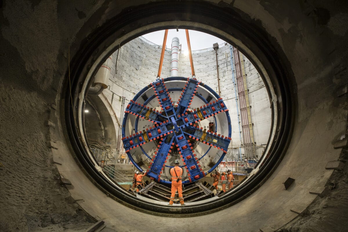 Northolt Tunnel 'Boring Machine' is lowered into place. It is a big round blue object being lowered in to a large round hole.