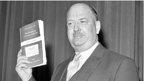 Dr Beeching holding up a British Railway book wearing a suit