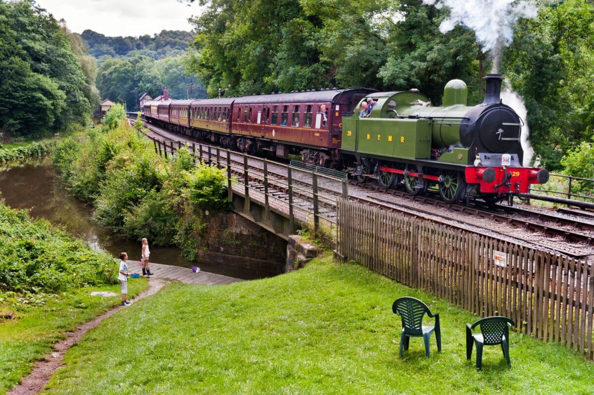 A steam train leaves Consall Station and crosses the Caldon Canal on the Churnet Valley Railway, Leek, Staffordshire, UK
