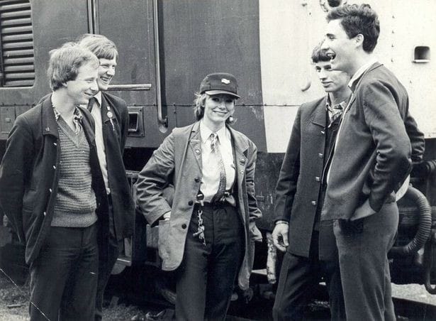 A black and white photo of Karen Harrison standing in front of a train, next to her male colleagues