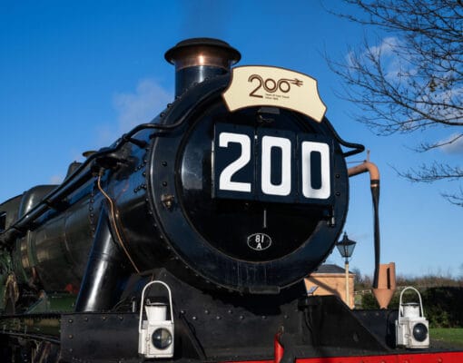 A train, at a platform, with a plaque on it's front that says Railway 200