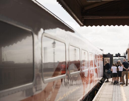 A train stationed on a platform with a group of children and teachers boarding it