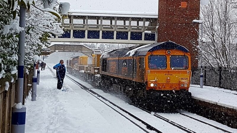 Freight train passing station in snow